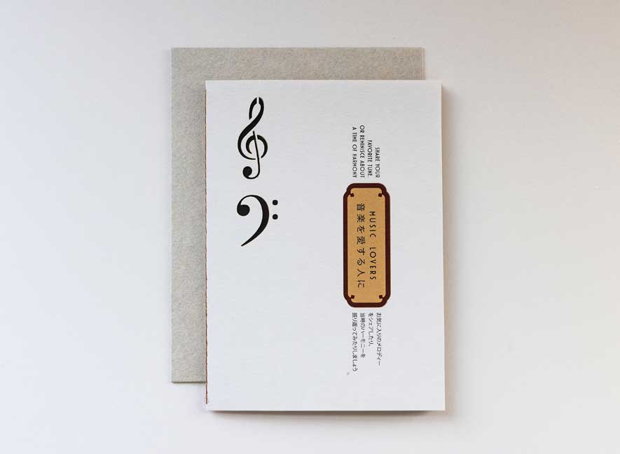 Luxury greeting card. Two-ply card using cream cotton cardstock with intricate treble and base clef cutouts on the exterior. Interior is smooth mustard-yellow paper with maroon accents and messages translated into English and Japanese.