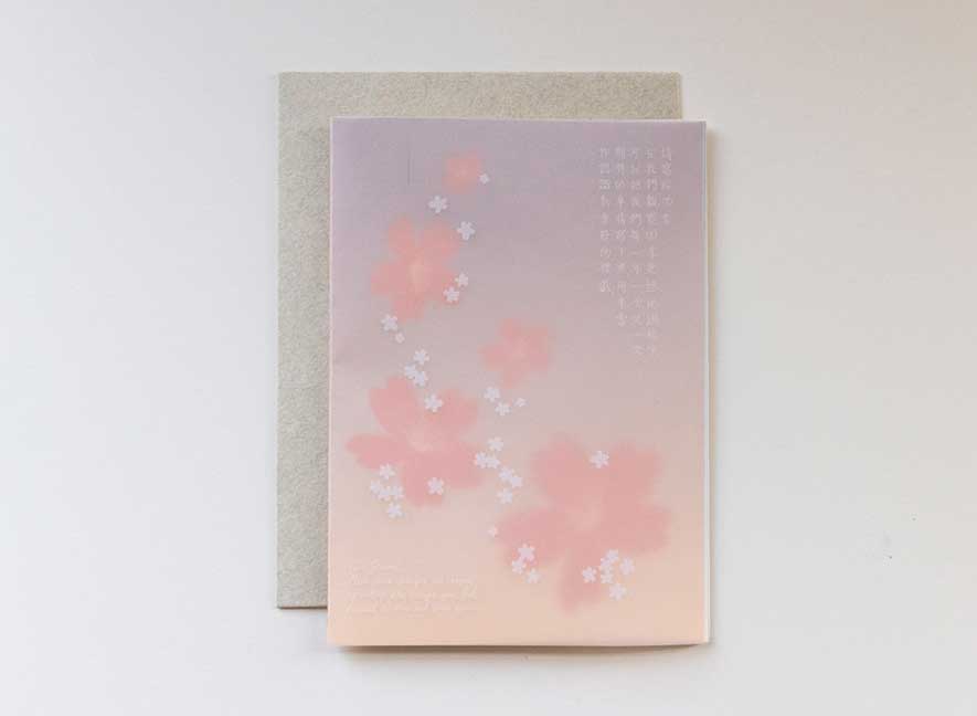 Luxury greeting card. Two-ply card with a translucent light pink cover printed with small white cherry blossoms that cascade throughout the paper. Interior is cream cardstock printed with blue skies larger and large white cherry blossoms that have been pressed into the paper. English-Chinese version.
