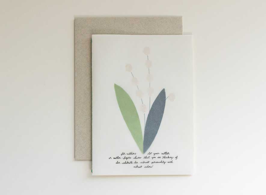 Luxury greeting card with a translucent cover and multi-language messages written on the surface in a cursive style evoking the art of handwriting letters. The interior of a card is an image of a lily of the valley, using different papers and printing styles to give the flower physical texture. English-only version.