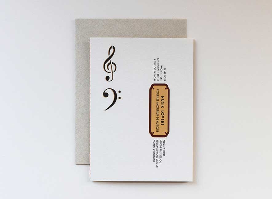  Luxury greeting card. Two-ply card using cream cotton cardstock with intricate treble and base clef cutouts on the exterior. Interior is smooth mustard-yellow paper with maroon accents and messages translated into English and French.