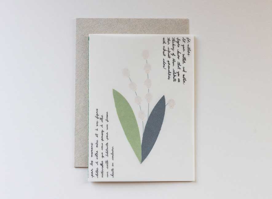 EN-FR| Luxury greeting card with a translucent cover and multi-language messages written on the surface in a cursive style evoking the art of handwriting letters. The interior of a card is an image of a lily of the valley, using different papers and printing styles to give the flower physical texture. English-French version.